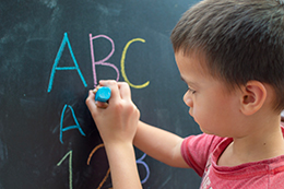 Un niño sujeta la mano de otro enseñándole a escribir. Enseñanza segura: cuidar los vínculos en el aula